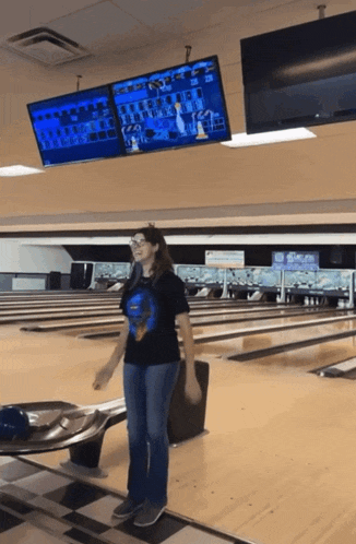 a woman stands in a bowling alley with a scoreboard above her that says ' strike '