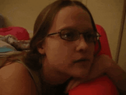 a woman wearing glasses is laying on a bed and looking at the camera