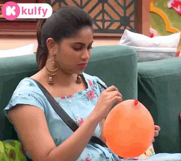 a woman is sitting on a couch holding an orange balloon with a k kulfy logo in the corner