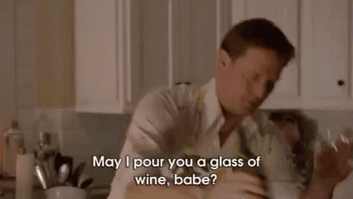 a man in an apron is holding a bottle of wine and a glass of wine in a kitchen .