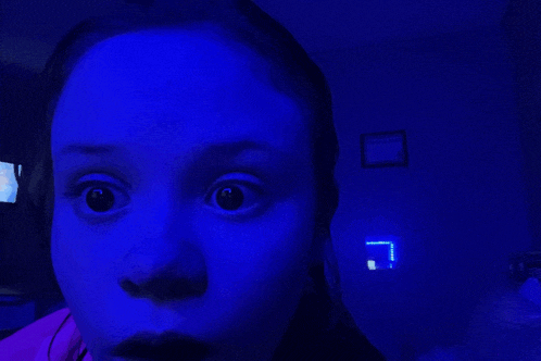 a girl with a surprised look on her face is standing in front of a blue light