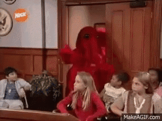a group of children are sitting in a courtroom with a red monster standing in front of them .