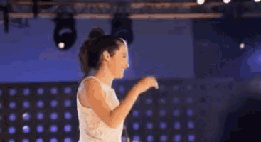 a woman in a white dress is dancing on a stage in front of a crowd .