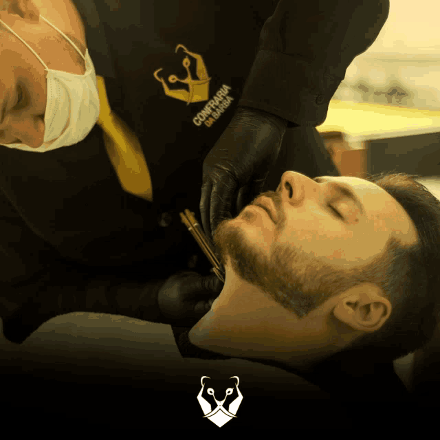 a man is getting his beard shaved by a man wearing a black shirt that says ' confiaria de barba '