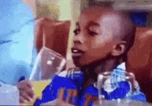 a young boy is sitting in a chair holding a can of soda and a glass of orange juice .
