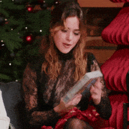 a woman in a black lace top sits in front of a christmas tree