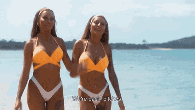 two women in bikinis are walking on a beach and one of them says we 're back bitches