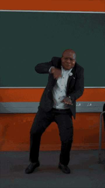 a man in a suit is dancing in front of a blackboard