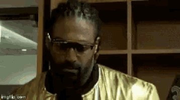 a man wearing glasses and a gold jacket is standing in front of a shelf .