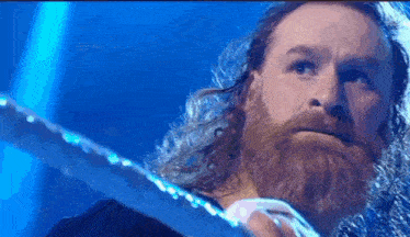 a man with a beard and long hair is holding a sword in his hands .