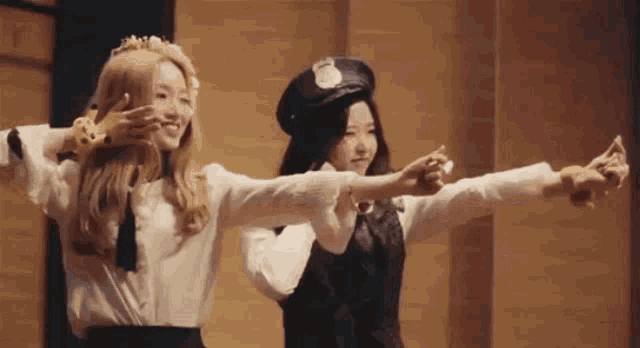 two women are standing next to each other with their arms outstretched in a room .