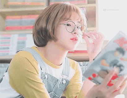a young woman wearing glasses is reading a book .