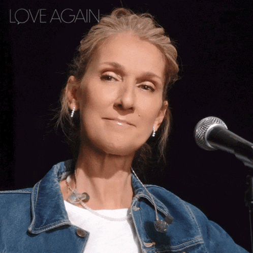 a woman in a denim jacket stands in front of a microphone with the words love again on the bottom