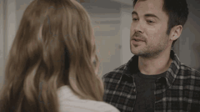 a man in a plaid shirt is talking to a woman in a white shirt