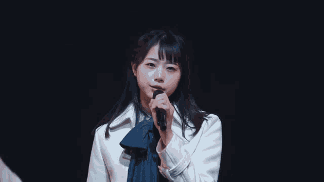 a girl in a white jacket is singing into a microphone on a stage
