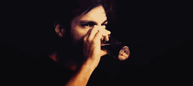 a man with a beard is drinking from a glass in a dark room .