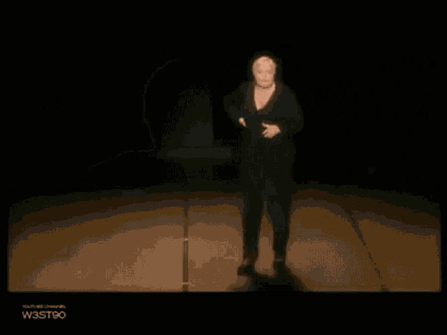 a woman in a black dress is standing on a stage with the words w3st90 at the bottom