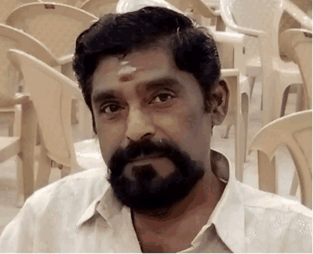 a man with a beard and a red spot on his forehead looks at the camera