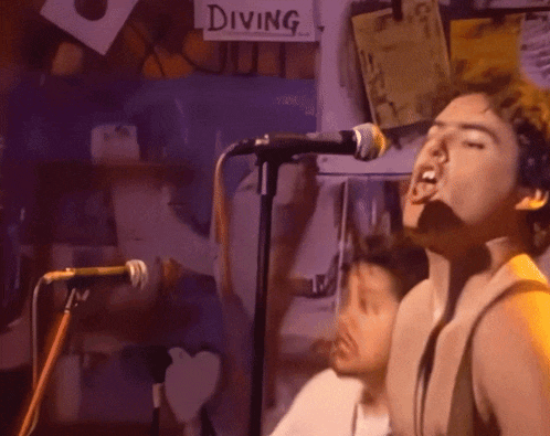 a man singing into a microphone with a diving sign behind him