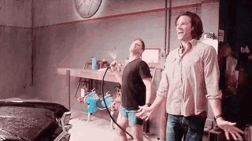 two men are standing next to each other in a garage with a hose .