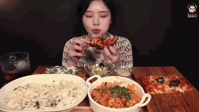 a woman is eating a slice of pizza while sitting at a table with bowls of food