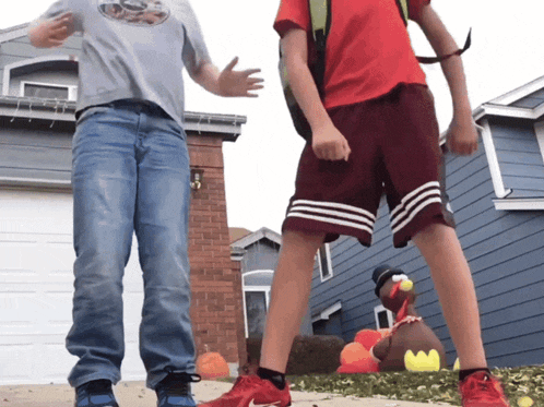 two boys standing in front of a house with a stuffed turkey in the background