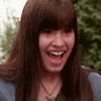 a woman with long brown hair and bangs is laughing with her mouth open .