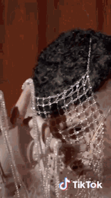 a tiktok video of a woman wearing a necklace with pearls on her face .
