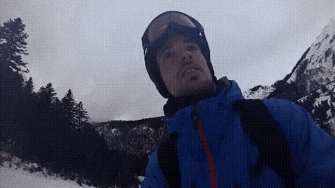 a man wearing a blue jacket and goggles is taking a selfie in the mountains .
