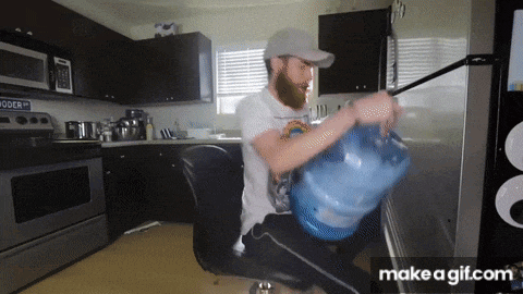 a man with a beard is carrying a large bottle of water in a kitchen ..