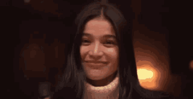 a close up of a woman smiling in a dark room with a fire in the background .