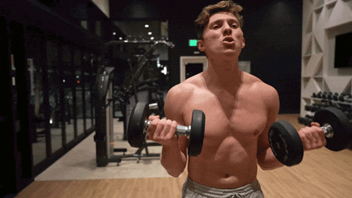 a shirtless man is lifting a dumbbell in a gym