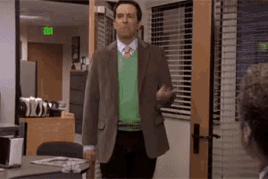 a man wearing a green sweater and a brown jacket is standing in front of an office door .