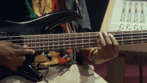 a man with dreadlocks is playing a bass guitar in front of a mixer