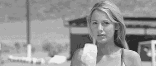 a black and white photo of a woman in a bikini eating an ice cream cone .