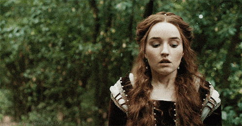 a woman with long red hair is standing in a forest with trees in the background and a tumblr logo in the corner