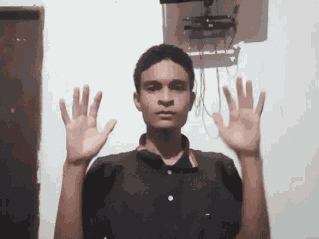 a young man in a black shirt holds his hands up in front of his face