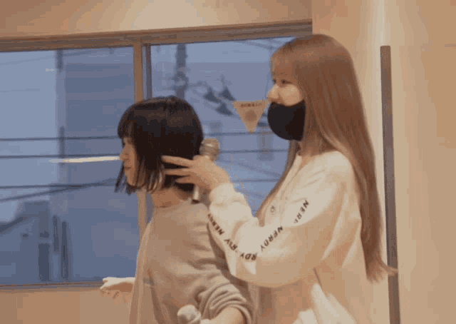 a woman wearing a nerdy boy sweatshirt holds a microphone over another woman 's ear