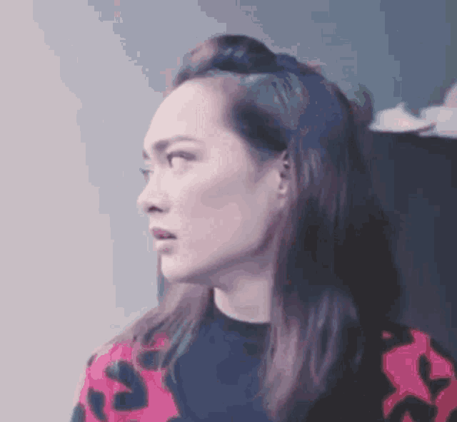 a woman with long hair is wearing a pink and black sweater and making a funny face .