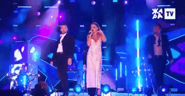 a woman in a white dress is singing into a microphone on a stage with a band .