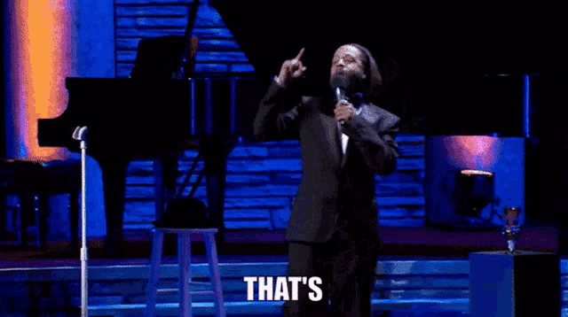 a man in a tuxedo is standing on a stage holding a microphone and says that 's .