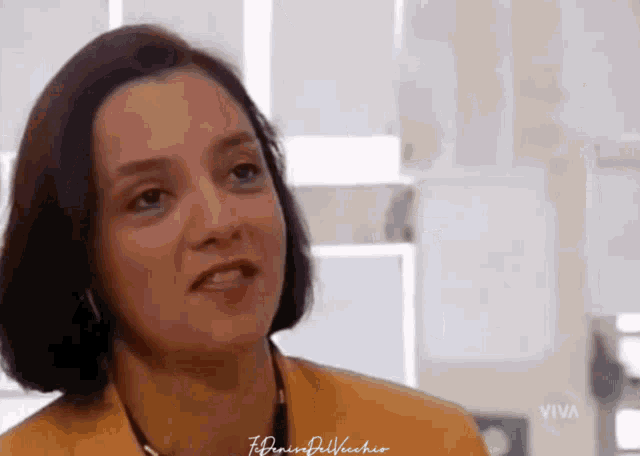 a woman is wearing a yellow jacket and a necklace and the word viva is on the bottom