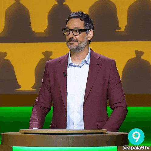 a man in a maroon suit is standing in front of a green podium with the number 9 on it