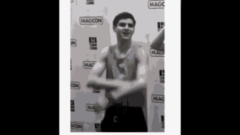 a man without a shirt is dancing in front of a wall that says magcon .