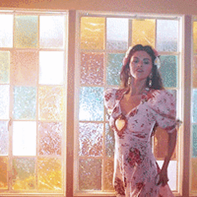 a woman in a floral dress is standing in front of a window with stained glass