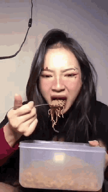 a woman eating noodles with a fork from a plastic container
