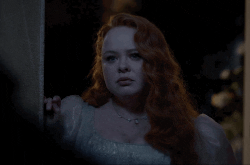 a woman with red hair and a white dress is standing in a dark room