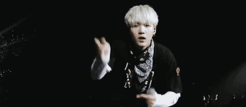 a young man with white hair and a bandana on his neck is making a funny face with his hands in the air .
