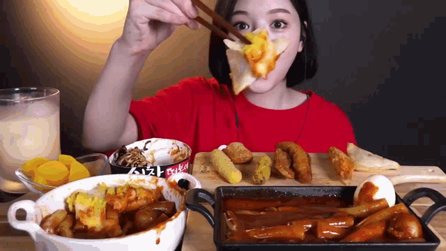 a woman in a red shirt is eating food with chopsticks and a can of sauce that says ' seoul ' on it