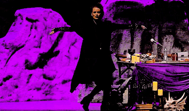 a woman in a black coat is standing in front of a microphone in a dark room with purple lights .